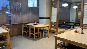 Interior de restaurante com mesas e cadeiras de madeira, uma janela grande e vista para o exterior.