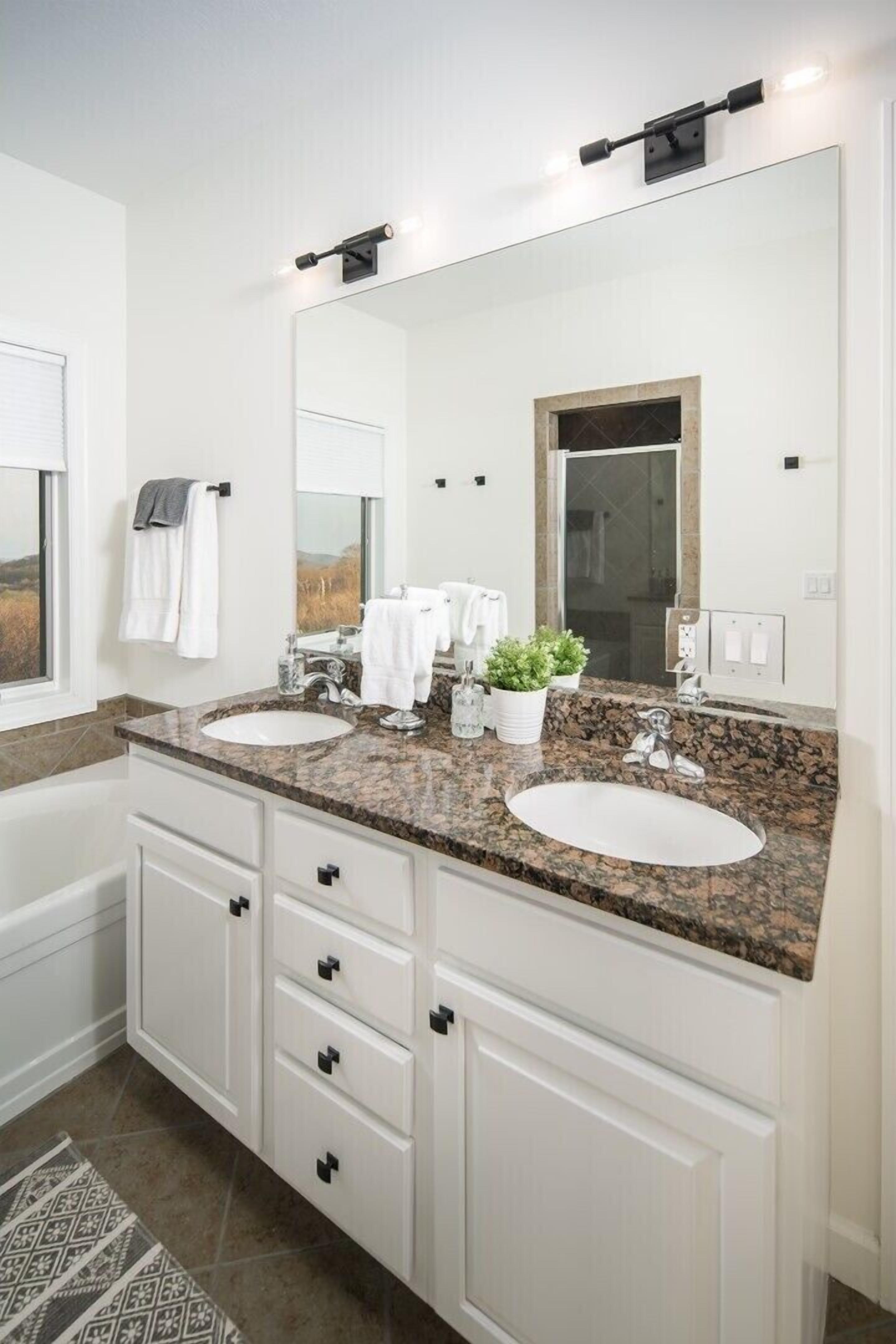 A modern bathroom with two sinks, a large mirror, and a window.