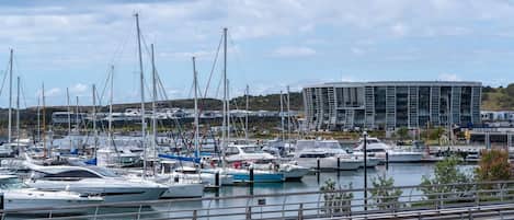 Un puerto deportivo con varias embarcaciones amarradas, un edificio moderno al fondo y un cielo despejado.