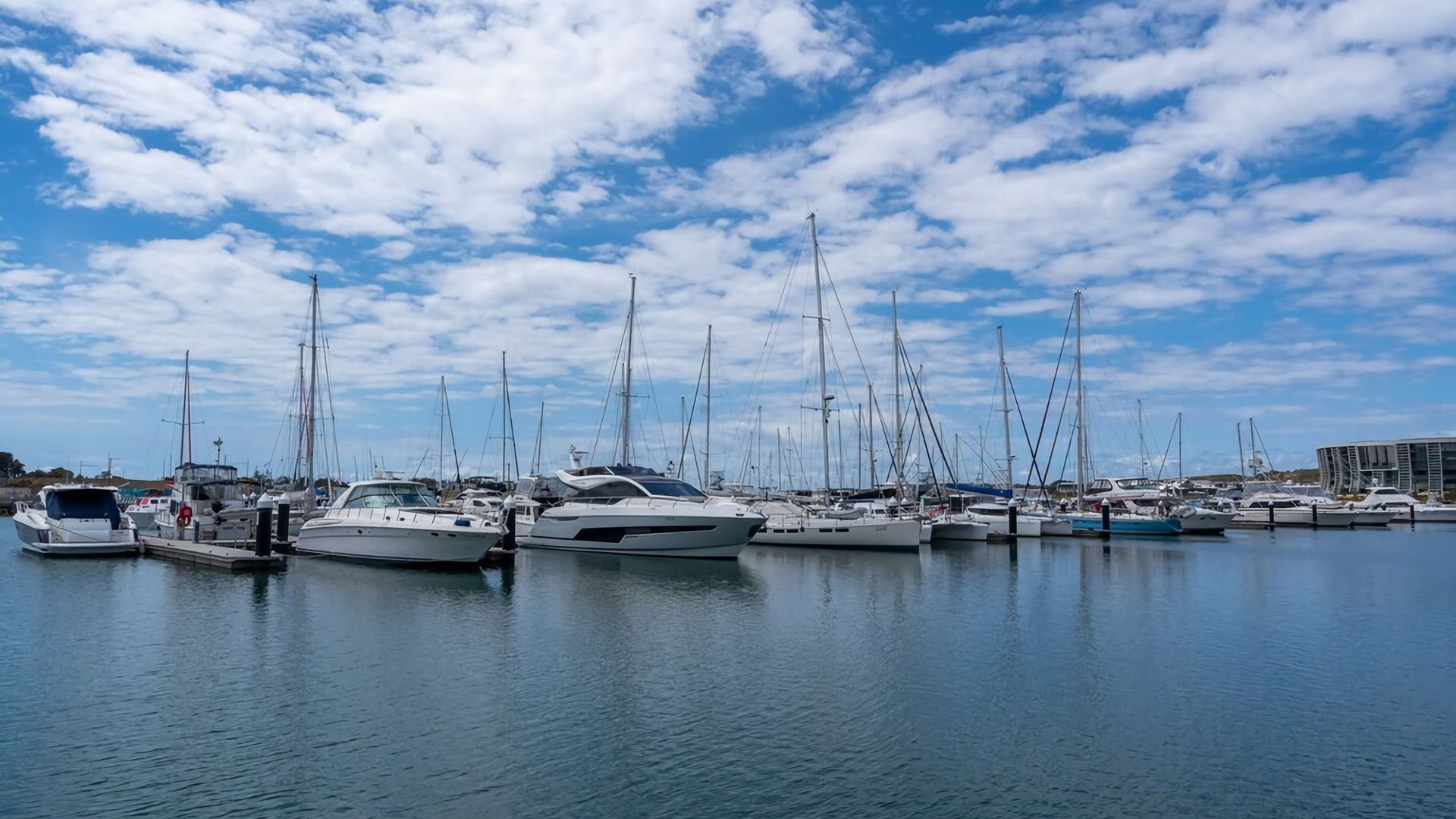 A marina with multiple boats docked, calm water, and a clear sky.