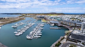 Un port de plaisance où sont amarrés de nombreux bateaux, un ensemble d’immeubles modernes et une vue dégagée sur la côte.