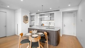 A modern kitchen with a central island, wooden chairs, and a dining table set for four. - Marina Getaway ~ Captivating 2-bedroom that accommodates up to 4 guests (Shell Cove)