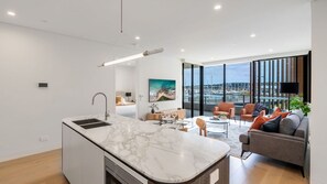 A modern kitchen with a marble countertop, a dining area with a round table, and a living space with a sofa and a view of the marina.