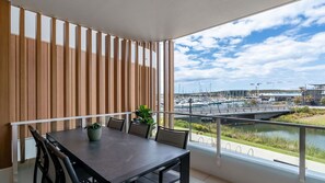 A balcony with a table and chairs, a view of a marina, and a wooden slatted wall. - Marina Getaway ~ Captivating 2-bedroom that accommodates up to 4 guests (Shell Cove)
