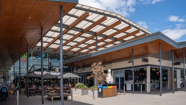 An outdoor seating area with tables and benches, a covered walkway, and a storefront with signage.