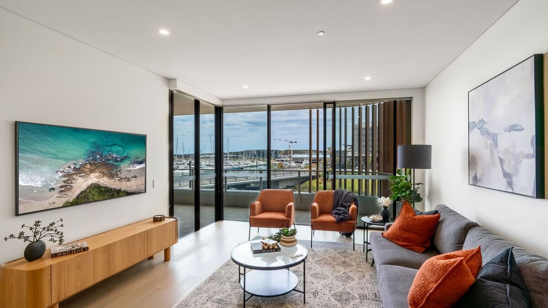 Un salon moderne doté d’une grande fenêtre, d’un canapé, de deux fauteuils, d’une table basse et d’une console sur laquelle est posée une plante.