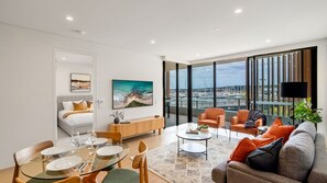 Sala de estar moderna com área de jantar, sofá e uma grande janela com vista para barcos.