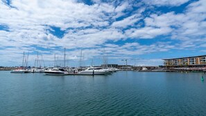 A marina with multiple yachts docked, a building with a modern design, and a clear sky with clouds.