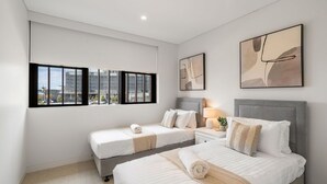 A hotel room with two beds, a nightstand, a lamp, and artwork on the walls. - Marina Getaway ~ Captivating 2-bedroom that accommodates up to 4 guests (Shell Cove)