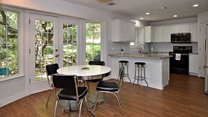 A modern kitchen with white cabinets, a central island with stools, and a dining area with a round table and chairs. - Dreamy Dripping Springs | Near Parks, Hiking & More! (Dripping Springs)