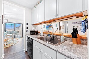 A kitchen with a granite countertop, stainless steel sink, white cabinets, and a view to a balcony. - Starfish Shore -2BD/2BA Condo with BEAUTIFUL Ocean Views (Myrtle Beach)