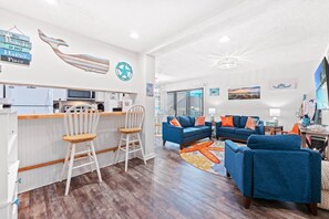 A modern living room with a kitchen area, featuring a bar, seating with cushions, and artwork on the walls. - Starfish Shore -2BD/2BA Condo with BEAUTIFUL Ocean Views (Myrtle Beach)