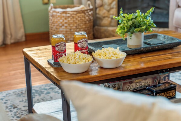 A wooden table with two bowls of popcorn, two cans of Snow Cap Cider, and a tray with a potted plant.