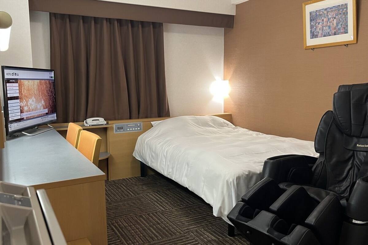Ein Hotelzimmer mit einem Bett, einem Massagesessel, einem Schreibtisch mit Computer und einem wandmontierten Fernseher.