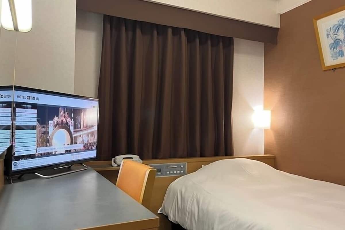 Ein Hotelzimmer mit einem Bett, einem Schreibtisch mit Computer, einem Telefon und einer Wandleuchte.