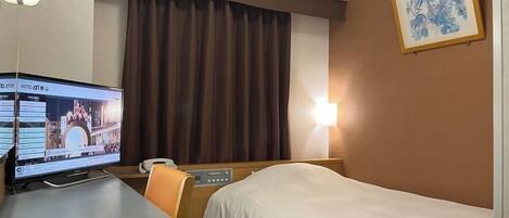 A hotel room with a bed, a desk with a computer, a telephone, and a wall-mounted light.