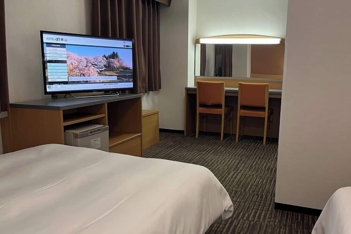 Ein Hotelzimmer mit Bett, Schreibtisch, Computer, Stuhl und Lampe.