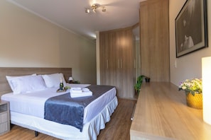 Una habitación de hotel moderna con una cama grande, un armario de madera y un pequeño escritorio con una lámpara.