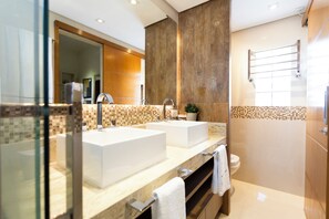 Un baño moderno con dos lavamanos, un espejo grande y cabina de ducha con mampara de vidrio.