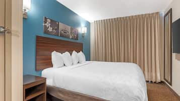 A hotel room with a bed, a wooden headboard, a nightstand, a wall-mounted TV, and a window with curtains.