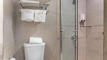 A modern bathroom with a glass shower enclosure, a toilet, a towel rack with towels, and a paper towel dispenser.