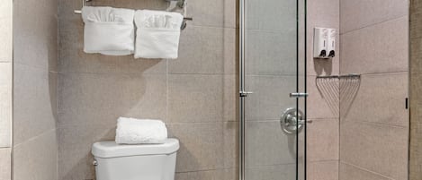 Un baño moderno con cabina de ducha de vidrio, un inodoro, un perchero con toallas y un dispensador de toallas de papel.