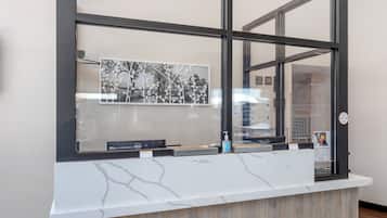 A reception desk with a marble top, a Dell computer, a bottle of hand sanitizer, and a framed picture of trees.