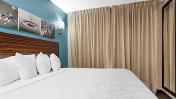 Una habitación de hotel con una cama grande, cabecera de madera, luz de pared y ventana con cortinas.