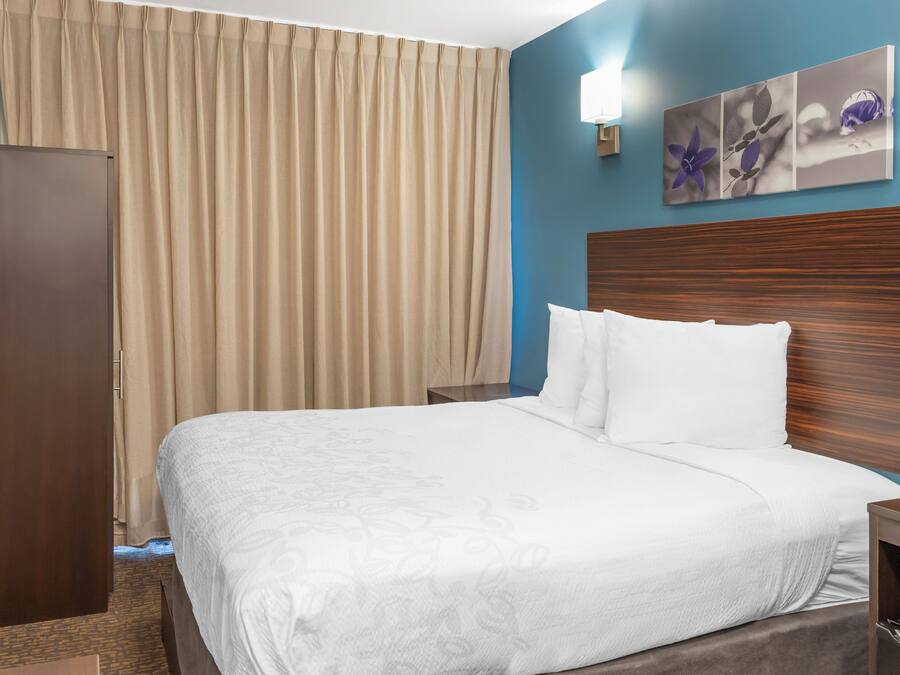 A hotel room with a bed, a wooden headboard, a nightstand, a wardrobe, and a window with curtains.
