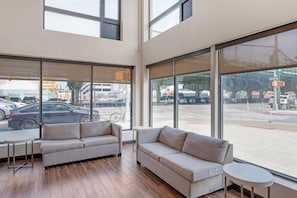 A modern hotel room with large windows, a sofa, a small table, and a view of the street. - Red Roof Inn PLUS+ Brooklyn - 3rd Ave (Brooklyn)