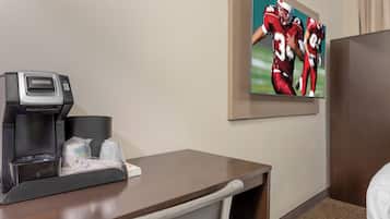 A hotel room with a desk, a coffee maker, a television mounted on the wall, and a bed.