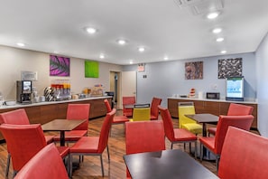 A modern cafe with red chairs, a coffee machine, and a counter with a menu. - Red Roof Inn PLUS+ Brooklyn - 3rd Ave (Brooklyn)