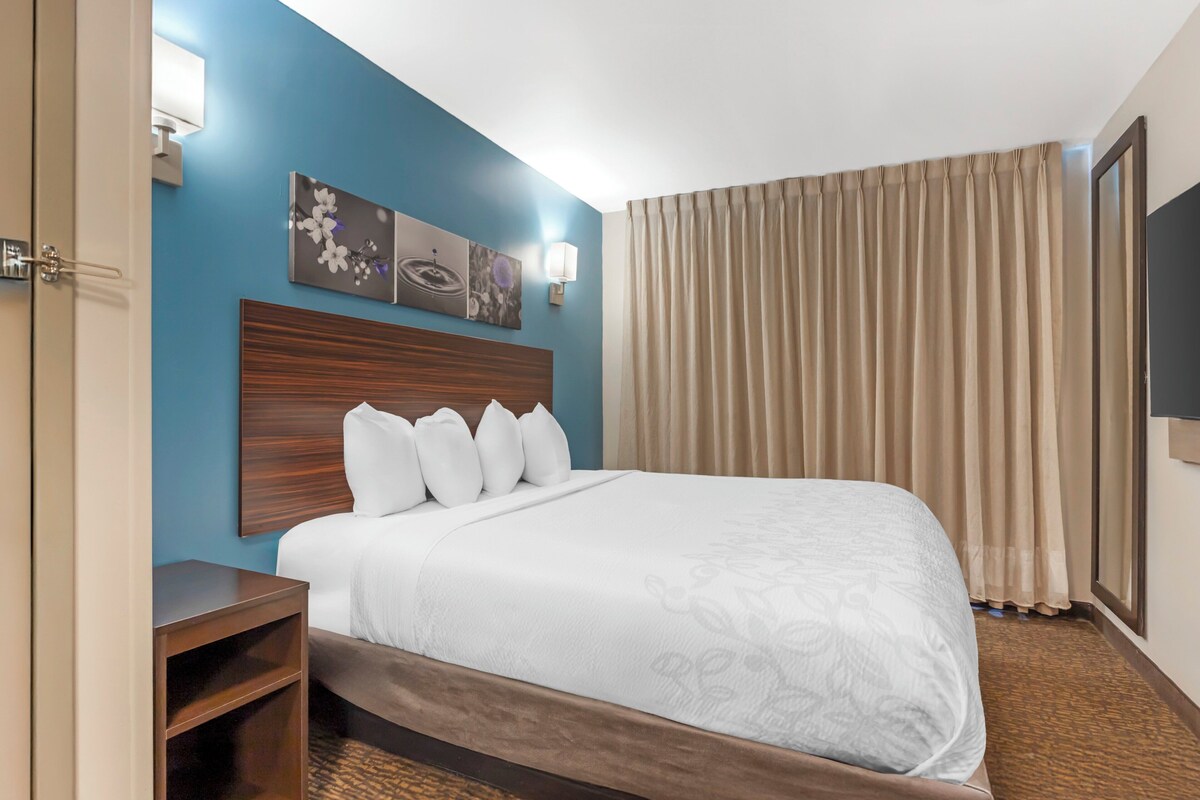 Habitación de hotel con una cama grande, cabecera de madera, mesita de noche y televisor montado en la pared.