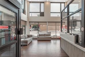 A modern interior with a sofa, a small table, and a large window overlooking a street. - Red Roof Inn PLUS+ Brooklyn - 3rd Ave (Brooklyn)