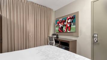 A hotel room with a bed, a television mounted on the wall, a desk with a chair, and a door with a privacy lock.