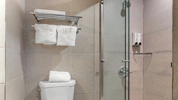 A modern bathroom with a glass shower enclosure, a toilet, and a towel rack with multiple towels. - Red Roof Inn PLUS+ Brooklyn - 3rd Ave (Brooklyn)