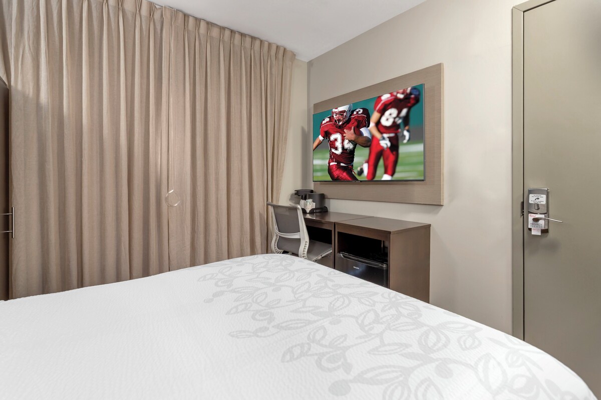 Una habitación de hotel con una cama, un escritorio, una silla, un televisor y una puerta.