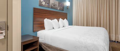 A hotel room with a bed, a nightstand, a wall-mounted lamp, and a window with curtains.