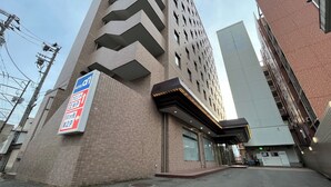 Un hotel con fachada de ladrillo moderno, un cartel que indica 50 metros de distancia al estacionamiento y un edificio grande al fondo.