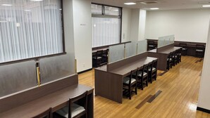 Un espacio de oficina moderno con amplias mesas de madera y separadores individuales, equipado con sillas y un gran ventanal con persianas.