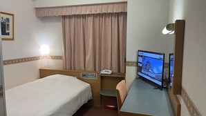 Una habitación de hotel con una cama individual, un escritorio con computadora, teléfono y ventana con cortinas.