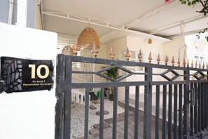 Une entrée fermée par un portail, avec une pancarte indiquant le numéro de la chambre (10) et un nom.