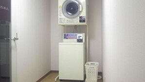 Un lavadero pequeño y funcional con lavadora y secadora apiladas, un refrigerador compacto y una cesta de ropa.