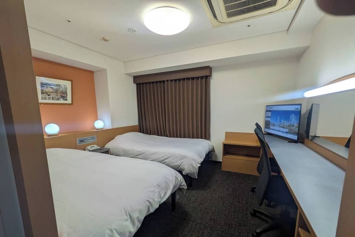Habitación de hotel con dos camas, un escritorio, una computadora y un televisor.