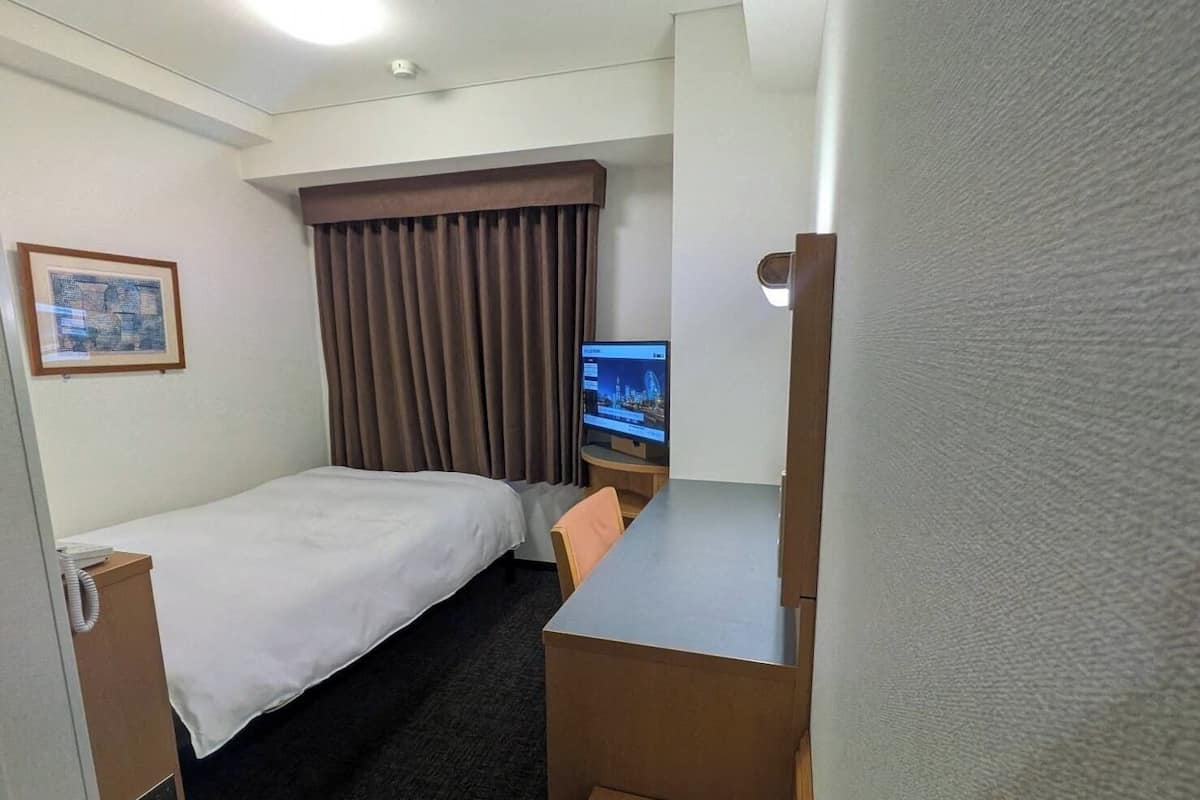 Una habitación de hotel con cama, escritorio, televisor y ventana con cortinas.