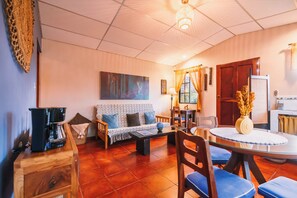 A living room with a sofa, coffee table, and chairs, a dining table with a vase, and a painting on the wall.