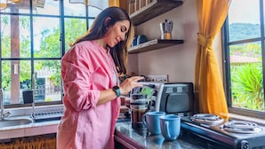 Une cuisine équipée d’une machine à café, une fenêtre avec des rideaux et une vue sur la verdure à l’extérieur.