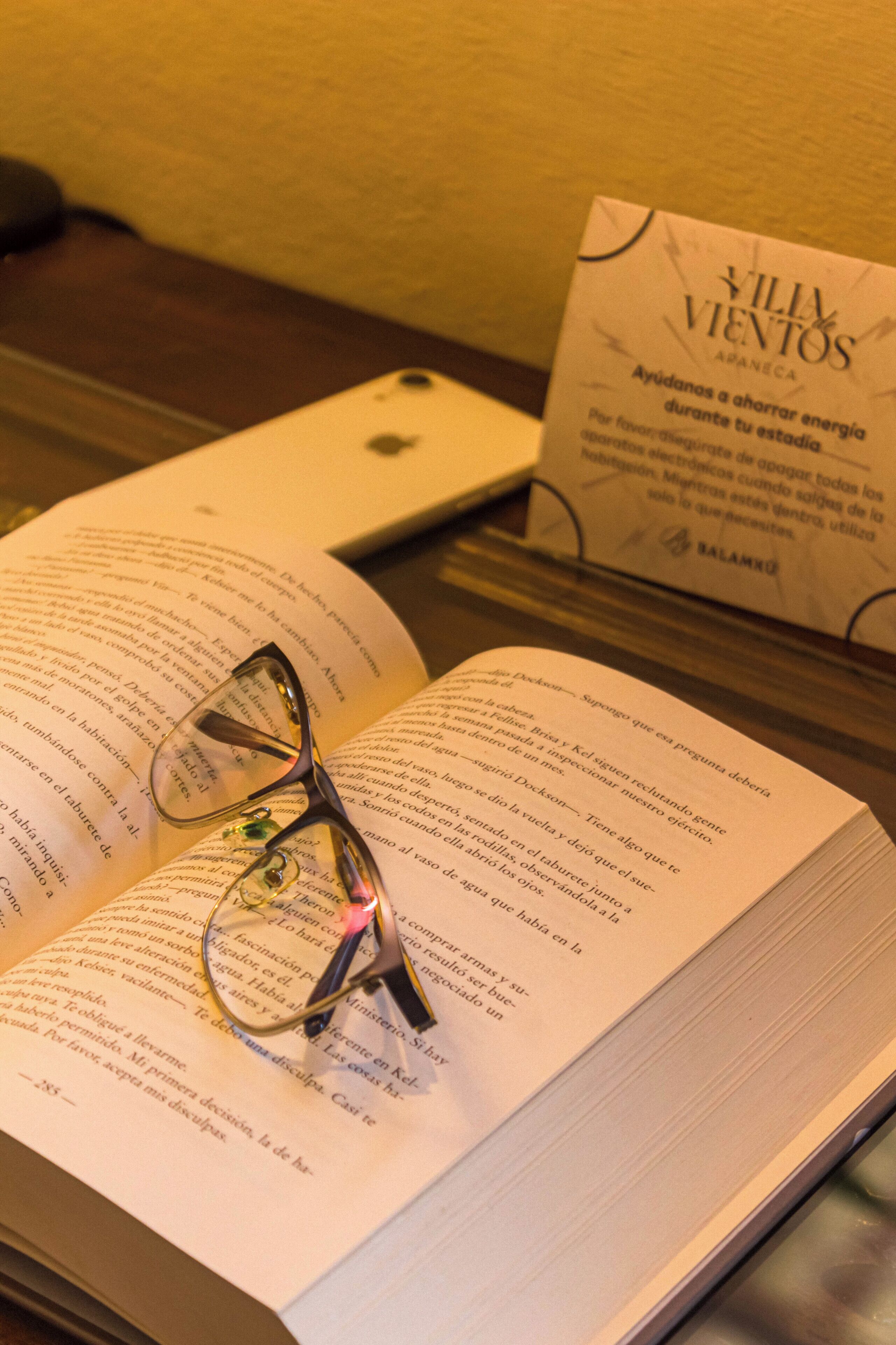 An open book with glasses on top, a business card, and a smartphone on a table.