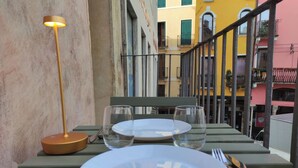 Une table dressée avec une assiette, deux verres et des couverts, sur un balcon offrant une vue sur des bâtiments aux couleurs vives.