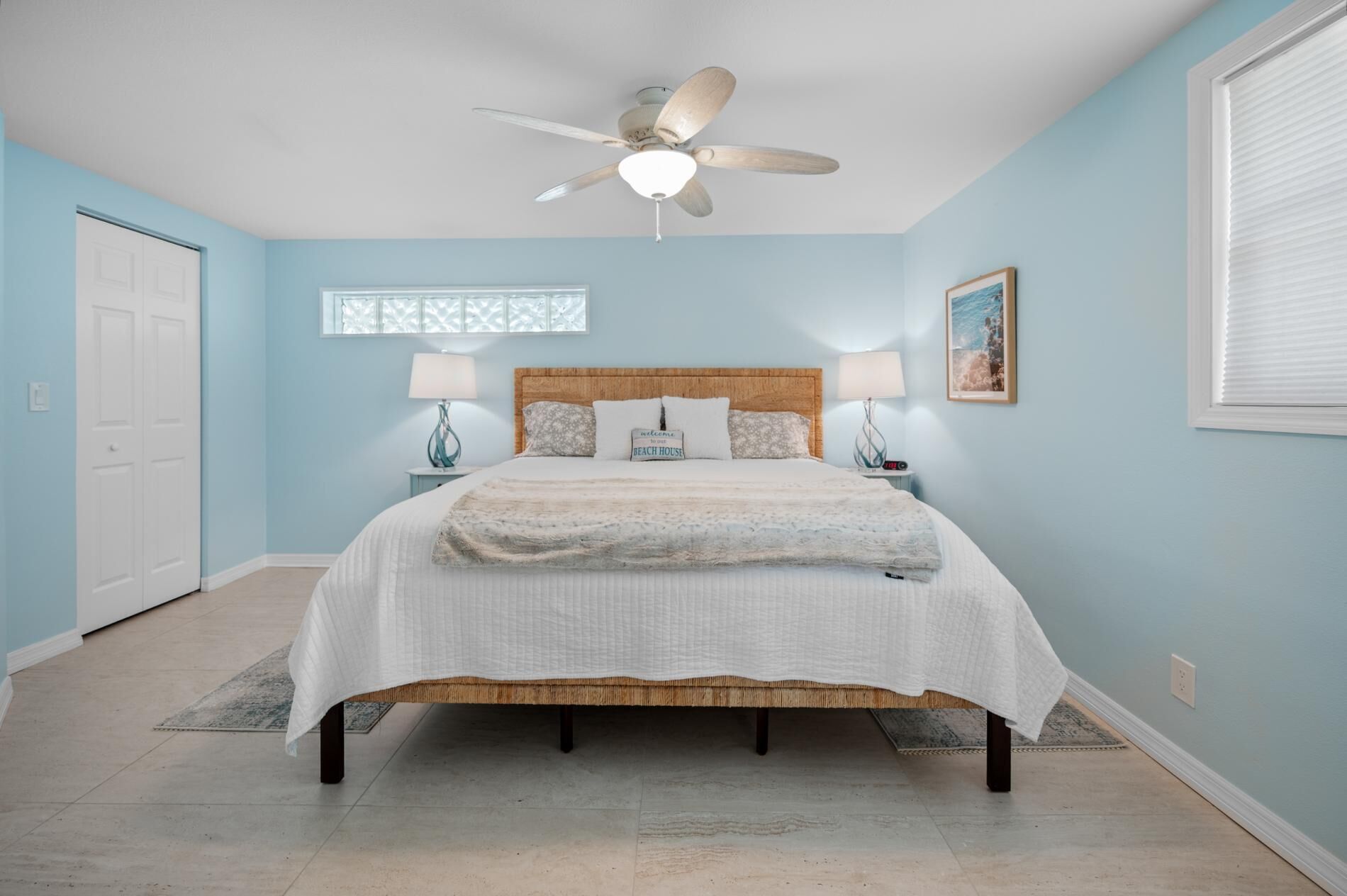 Une chambre à coucher comprenant un lit, deux tables de chevet, un ventilateur de plafond, une fenêtre avec vue et une porte.